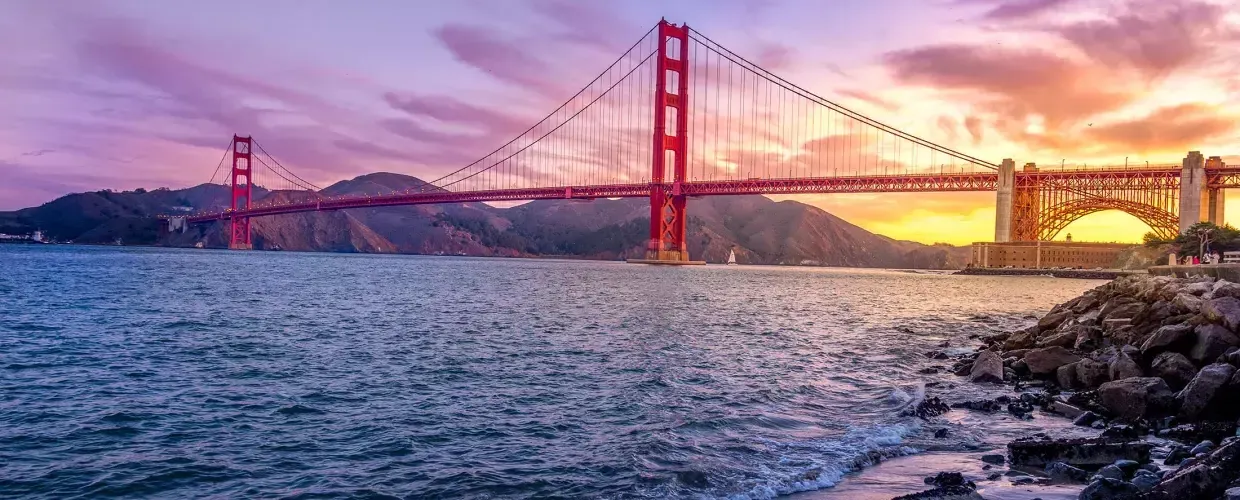 The 金门大桥 at sunset with a multicolored sky 和 the San Francisco Bay in the foreground.