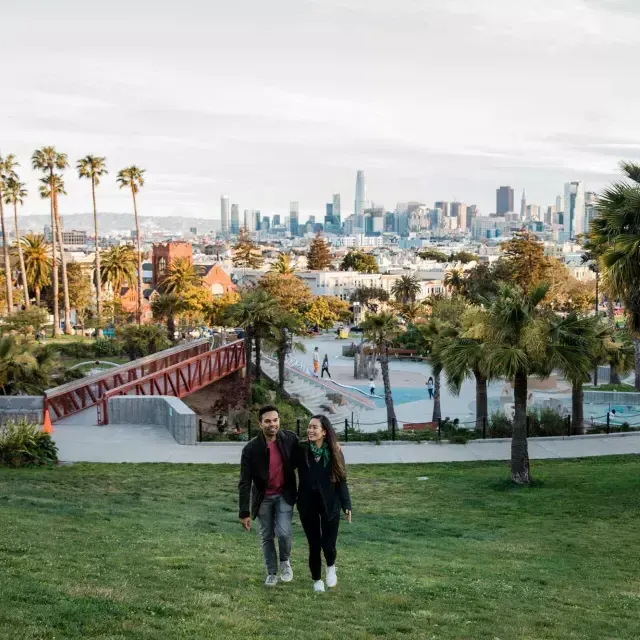 A couple walks toward the camera with 德洛丽丝公园 和 the San Francisco Skyline behind them.